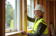 © Maryna - Middle-aged male construction worker installs windows. Caucasian pro wears hard hat, reflective vest. Home renovation building interior with wood frame, glass windows. Improvement, repair,