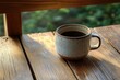 © btiger - A rustic ceramic cup filled with coffee sitting on a sunlit wooden table near a window with a blurred green outdoor background