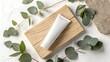 © PhotoHub - Minimalist flat lay of a white cosmetic tube on a wooden board surrounded by eucalyptus leaves and a stone