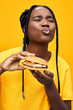 © SHOTPRIME STUDIO - Happy young woman enjoying a burger with a playful expression against a vibrant yellow background, showcasing comfort food and joy in a trendy, colorful style