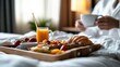 © AspctStyle - Deluxe breakfast tray with fresh croissant, fruit, orange juice, and coffee served on bed in cozy hotel room with guest in bathrobe. Morning indulgence and luxury hospitality concept.