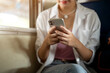 © bongkarn - Close up of woman holding phone with both hand looking or typing as sitting on train carriage bench.