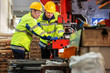 © BESTIMAGE - Two male industrial workers wea safety helmets and reflective jackets operating large industrial machinery in a factory setting with tools and equipment around