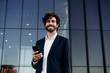 © Westend61 - Smiling businessman with smart phone in front of building