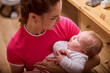 © TRAVELARIUM - Young woman with brown hair cradles infant girl, evoking warmth and comfort. Soft indoor light highlights intimate moment, creating serene atmosphere around them