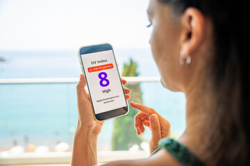 young woman checking uv index on smartphone with high radiation alert. mobile app warns to apply sun