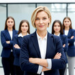 © Mdhittu - A confident blonde businesswoman stands in front of a team of female colleagues, all with their arms crossed, in a modern office
