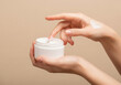 © PictoAi - A pair of hands holding a jar of white skincare cream, one hand squeezing out a small amount of cream
