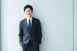 © nakayama - 白い壁を背景に微笑むスーツ姿の若手ビジネスマン
