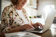 © Marko Geber - Senior woman managing finances online at home kitchen table