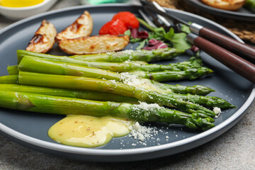 Wall Mural - Tasty cooked asparagus served with baked potatoes, tomatoes and sauce on grey table, closeup