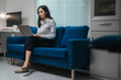 © PaeGAG - Asian businesswoman working from home sitting on a blue sofa using laptop in home office