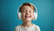 © miss irine - Happy boy wears headphones listens music with eyes closed. Smiling child enjoys audio entertainment in peaceful indoor setting. Joyful face portrait against blue background. Childhood concept.