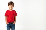 Cute brunette boy in red t-shirt smiles on white background. Happy kid with hands in pockets. Child portrait with cheerful expression. Joyful youth in studio shot.