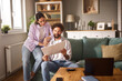 © Stockphotodirectors - A couple sits on a couch in their living room, engaged in a discussion about life insurance while reviewing documents. Natural light fills the room, creating a warm atmosphere.