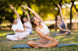 © JackF - Smiling young girl in white sports top and beige shorts sitting in lotus position during group yoga class in sunny park, concentrating on muscle stretching