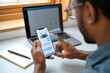 © NOSOX - African American man using AI chatbot app on smartphone, laptop in background, modern workspace, professional, focused.