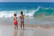 © Tropical studio - Happy kids have fun in sea surf on white sand beach. Couple of children sit in water pool. Travel lifestyle, swimming activities in family summer camp. Vacations on tropical island.