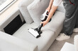 © Pixel-Shot - Male janitor with modern handheld vacuum cleaner cleaning sofa in room