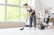 © Pixel-Shot - Young male janitor with modern vacuum cleaner cleaning floor in room