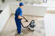 © Pixel-Shot - Young male janitor with modern vacuum cleaner cleaning carpet in kitchen