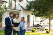 © zinkevych - Real estate agent presenting clipboard with documents to couple in front of residential property