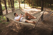 © illustrissima - Father and son 5 years old fooling around playing relaxing in a hammock outdoors in a pine forest at a campsite. Tourism, active recreation, time spent with children