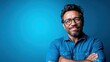 © Freshpixel - A confident middle-aged man with charming glasses smiles warmly against a vibrant blue background, showing an expression of positivity and approachability in a modern setting.