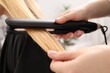 © New Africa - Hairdresser straightening woman's hair in salon, closeup