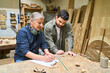 © Robert Kneschke - Experienced craftsman instructing young apprentice in woodworking shop