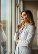 © NoelMatic - Thoughtful female doctor in white coat with stethoscope looking out a hospital window. Portrait of a hopeful and caring healthcare professional or general practitioner in a clinic.