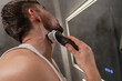 © blackday - Man shaving his face with a rotary electric razor while looking into a mirror