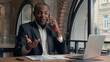 © Yuliia - Multitasking busy African American entrepreneur with laptop computer paperwork check data in papers business man office businessman male guy executive talking mobile phone smartphone call conversation