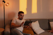 © blackday - Man Browsing Tablet on Sofa During Cozy Evening at Home