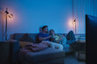 © blackday - Couple watching TV at night  while sharing a bowl of popcorn and wine on sofa