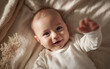 © Korkiat - A cute baby lying on the bed, smiling and waving their hand in joy. The background is beige linen with some dried grass, and the baby is wearing a white long-sleeved onesie.