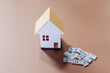 © aerogondo - Model house with scattered money on a brown surface representing financial investment in real estate