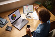 © Stockphotodirectors - A person is working in a home office, analyzing charts and presentations on a laptop and tablet, while sipping coffee. Papers and a calculator are nearby.