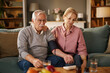 © Stockphotodirectors - An elderly man checks his blood pressure with an automatic monitor while sitting on a couch. His wife sits next to him with her hand on his shoulder, appearing worried.