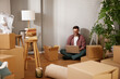 © Stockphotodirectors - A man sits on the floor of his new living room, working on a laptop amidst unpacked boxes and books. Sunlight streams through the window, adding warmth to the space.