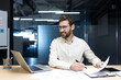 © Tetiana - Smiling young businessman working in the office with documents, talking on a video call and holding an online conference with partners