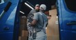 © Framestock - Outside of Logistics Warehouse: Male Employee Unloading Delivery Truck with Cardboard Boxes, Online Orders, Purchases and E-Commerce Goods. African American Manager Using Digital Tablet. Slow Motion.