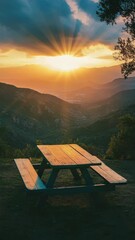 Wall Mural - Wooden picnic table on hilltop with sun rays through clouds at sunset