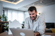 © Migma_Agency - Architect smiling and working on laptop with house model on table