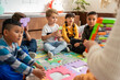 © Alan - Group of preschool children sitting on the classroom floor while the teacher uses an abacus to explain basic math. Kindergarten early education encourages curiosity and hands-on number learning