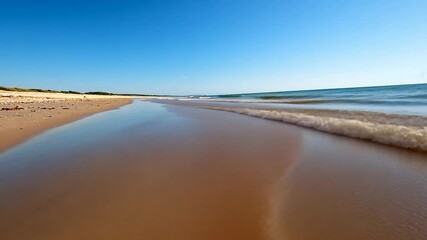 Wall Mural - coastal scene depicting a sandy beach with gentle waves under a bright blue sky. the water reflects 
