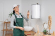 © Pixel-Shot - Female worker with flexible hoses near modern electric boiler in bathroom