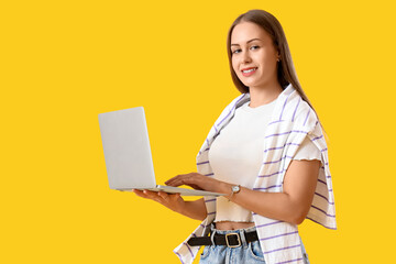 young woman using modern laptop on yellow background
