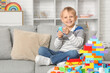 © Pixel-Shot - Happy cute little boy playing with colorful toy bricks on sofa at home