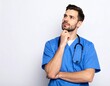 © fian - A thoughtful male healthcare professional in blue scrubs and a stethoscope is shown thinking deeply, likely contemplating a medical matter, in a studio or clean professional setting.